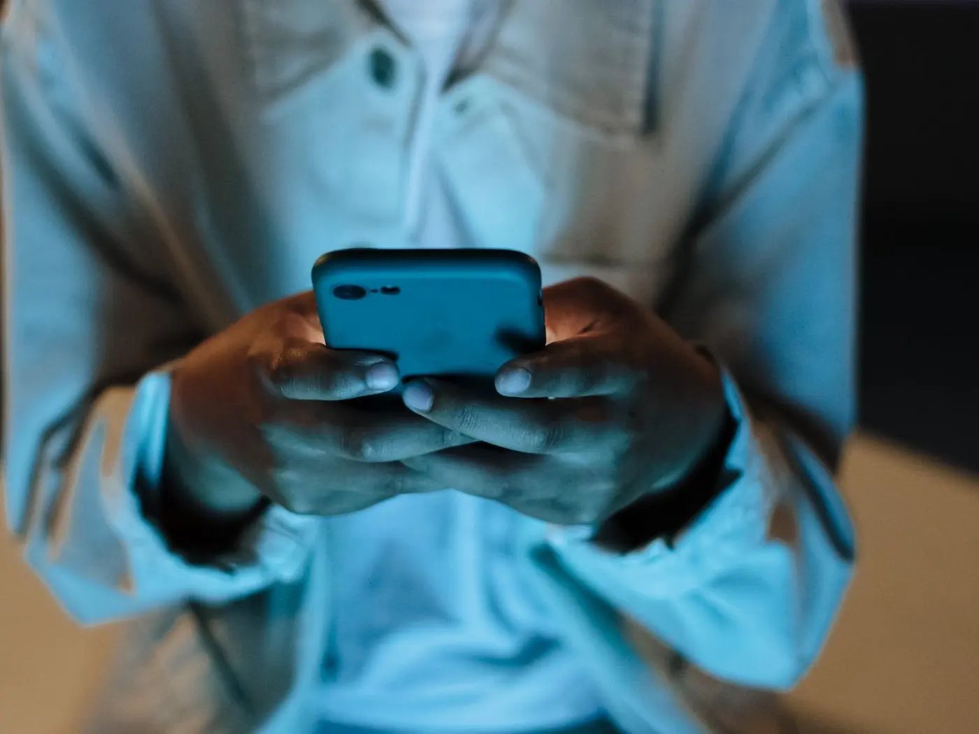 Hands typing a single line on a phone lit by its own screen at night.